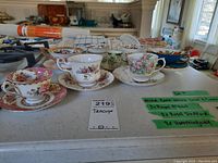 Seven bone china floral teacups and saucers with one small espresso cup and saucer displayed on counter.