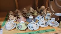Multiple teacups and saucers, teapot, creamer, and sugar bowl displayed showing variety of floral patterns and colors