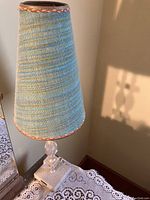 Photo of vintage lamp with crystal and metal base and tall tapered blue fabric shade with brown trim on lace covered surface