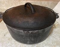 Front view of the antique cast iron pot with lid on, showing the curved handle on lid and clean exterior.