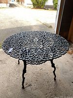Photo showing full view of the cast iron table with intricate openwork design and three curved legs.