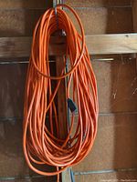 Long coiled orange extension cord hanging on a wooden beam in garage.