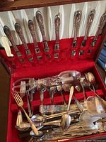 Silver plated forks and spoons in a red-lined wooden box with various cake-cutting utensils