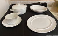 Full set displayed together on black cloth: casserole dish with lid, gravy boat on plate, two serving bowls, and serving platter.