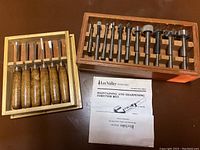 Photo of chisels with wooden handles arranged in tray alongside a wooden tray holding Forstner bits and an instruction sheet.