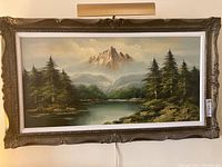 Full view of framed oil painting depicting mountain landscape with lake and trees.