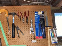 Hand tools arranged hanging on pegboard showing hammer, pliers, adjustable wrenches, pipe cutter, hacksaw, precision screwdriver set.