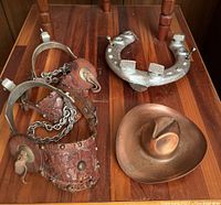 Overview of the lot displaying the pair of spurs, horseshoe, and brass cowboy hat on a wooden surface.