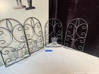 Four black metal scrollwork wall art tea candle holders together. One is missing the glass candle holder cup.