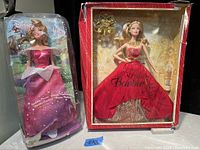 Two dolls in their boxes, Holiday Barbie in red and gold gown and Disney Sparkling Princess Barbie in pink dress.