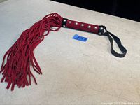 Red suede whip with long tassels and studded handle lying flat showcasing tassels and loop