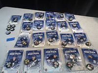 Photo of 21 mini hockey pucks in original sealed packaging and 5 loose mini pucks, all Toronto Maple Leafs themed, arranged on a white table.