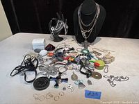 Full view of assorted lot on table showing variety of costume jewelry and some sterling silver pieces including bracelets, necklaces, charms, and earrings.