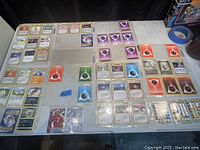Multiple assorted Pokemon cards spread on a table showing energy, trainer and Pokemon character cards along with baseball and Trash Pack cards in sleeves.