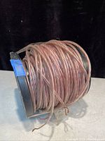 A spool of heavy duty clear insulated speaker wire coiled around a black plastic reel with blue tape labeling.