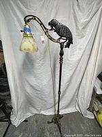 Full view of the antique bridge lamp showing brass stand, curved arm, glass shade, and cast iron parrot.
