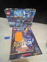 Photo showing LEGO Marvel set box 76113 featuring Spider-Man, Venom, and a red vehicle along with a LEGO Nexo Knights pamphlet titled 'Clash, Boom, Bang!'