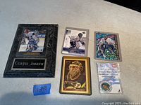 Five Curtis Joseph Toronto Maple Leafs collectibles spread on a white surface, including one black plaque and four hockey cards.