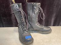 Pair of black leather Dr. Martens boots standing side by side showing front lace-up and side zipper.