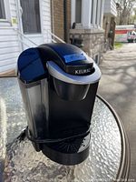 Front and angled view of the black Keurig coffee machine showing water reservoir, dispensing area, and control buttons.