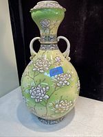 Front view of the large antique Satsuma vase showing the pale green ground with white raised floral decorations and two handles.