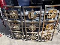 Three vintage metal wall art panels displayed outdoors on a vehicle tailgate, showing overall appearance and design.