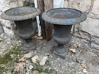 Pair of cast iron urn planters side by side against stone wall