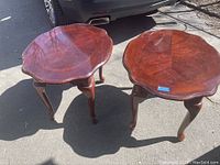 Pair of oval wooden end tables with scalloped edges and cabriole legs shown in the sunlight.