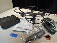 Photo showing the black quadcopter drone with propeller guards, the DX-3 remote controller, instruction sheet, and sealed bags containing spare parts and accessories.