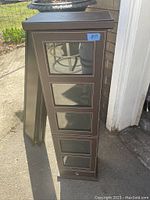 Front view of tall slim cabinet showing four mirrored drawer fronts and single drawer below.