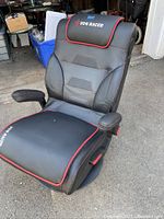 Front angled view of the black and red VON Racer gaming chair showing ergonomic padding, seat, and flip-up armrests.