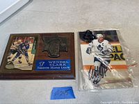 Wooden plaque with metal Toronto Maple Leafs emblem and blue nameplate for Wendel Clark, alongside a signed photo of Wendel Clark in hockey gear inside plastic sleeve.