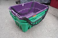 Two stacked plastic shopping baskets, one purple and one green, with black carrying straps.