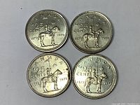 Four Canadian 25 cent coins showing the RCMP Centennial side with Mountie on horseback and inscriptions 'CANADA 25 CENTS 1873 1973'