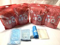 Four sealed red MY Tagalongs Road Trip Smart Kit packs standing. Plus contents laid out: blue disposable mask, wipe packet, small hand sanitizer bottle, blue garbage bag roll, disposable toilet seat cover.