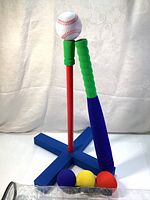 Full view of assembled T-ball set including the tee, bat, white foam baseball on tee, and the three colored foam balls (purple, yellow, red) on the ground nearby.