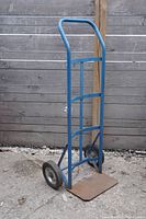 Full view of blue metal dolly trolley cart with two black wheels, standing upright on concrete.