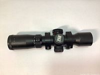 Side view of the black Excalibur Tact 100 scope showing adjustment turrets and label.