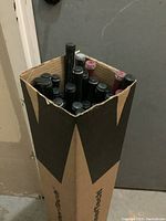 Box filled with golf shafts seen from the top showing mostly shaft ends and grips inside a tall rectangular cardboard box.