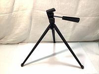 Full view of the black metal lightweight table top tripod showing three legs spread out and stable stance.