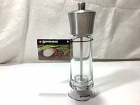 Front view of Swissmar 8-inch salt and pepper mill with acrylic body and metallic top and base, showing internal grind rod and product tag attached.