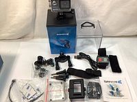 Photo showing Safari 3 4K action camera mounted on its display box along with all included accessories - waterproof housing, mounting brackets, wrist remote strap, charging cable, and user manual.