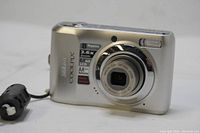 Front view of Nikon Coolpix L19 showing product labels on silver body, lens details, and flash