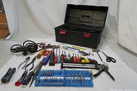Photo showing open tool box with tools arranged around it including screwdrivers, pliers, bits, caulking gun, scissors, and other tools