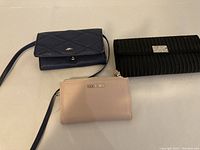 Three small purses laid on a surface: navy blue quilted purse, black textured clutch with rhinestone buckle, blush pink purse