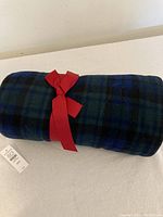 Rolled Blackwatch tartan throw blanket tied with a red ribbon, showing the plaid pattern and price tag.