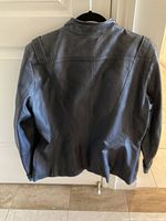 Back view of navy blue leather jacket hanging on hanger. Shows smooth navy leather with shoulder seam details and a short length ending just below the waist.