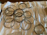 Silver and metal bangles and bracelets of varied designs laid out on a white cloth.