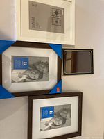 Photo of four new picture frames arranged side by side: a large white frame, a medium blue bordered frame, a smaller dark brown frame, and a small black and gold frame.