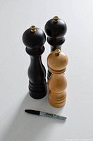 Three Peugeot salt grinders placed upright alongside a Sharpie for size scale, two dark wood and one light wood color.